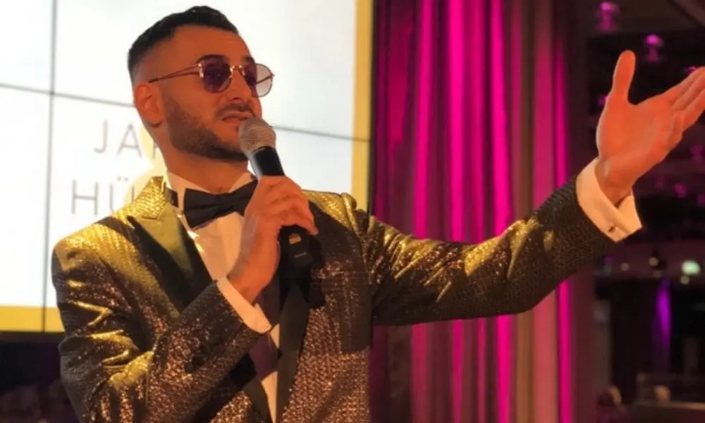 Tamada Daniel im goldenen Sakko auf der Bühne - WeddingBro Events Moderator Daniel mit dem Brautpaar